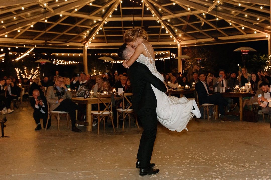 Groom lifting the bride during their first dance under string lights