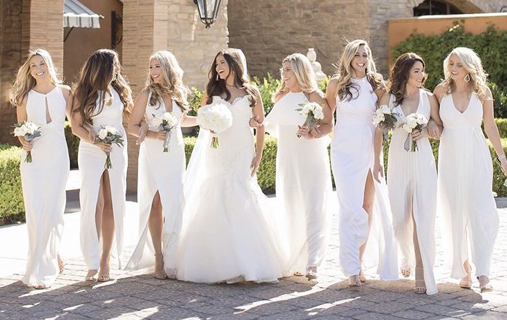 Bride walking arm in arm with bridesmaids in white